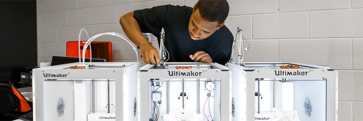 A lab technician prepares one of three 3D printers for 3D modelling.