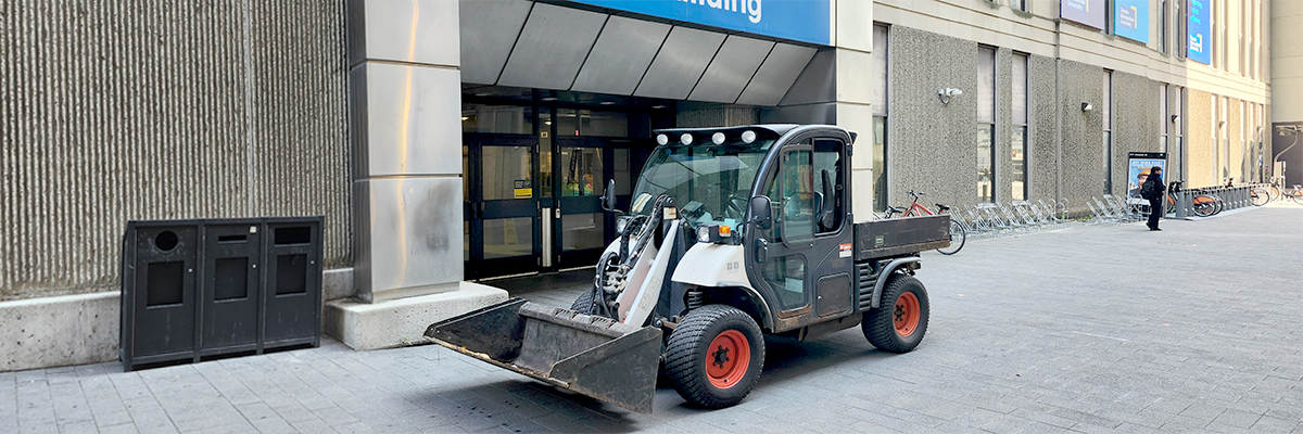 A small facilities vehicle used for moving earth or snow is shown parked in front of the Victoria Building.