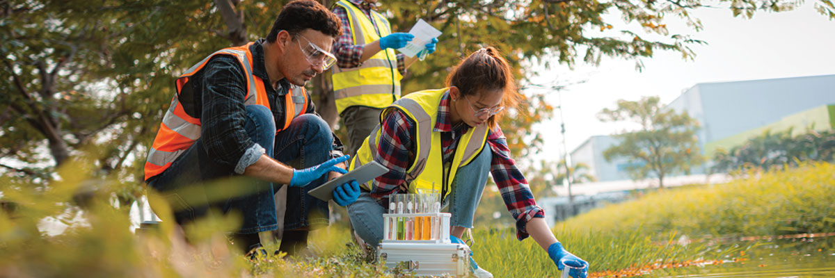 A diverse group of students in PPE takes water samples from a wetland near and industrial park.