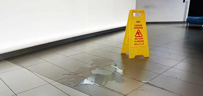 Liquid spill on tiled floor with a yellow caution sign next to it so people are alerted to the hazard.