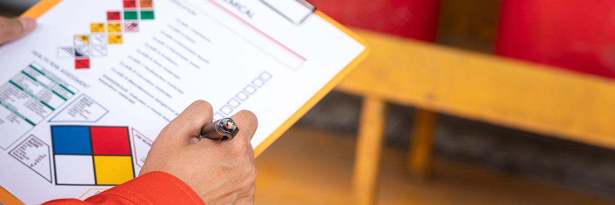 A close-up of a hand holding  pen to check off the hazards listed on a form prior to the loading of of hazardous chemicals.