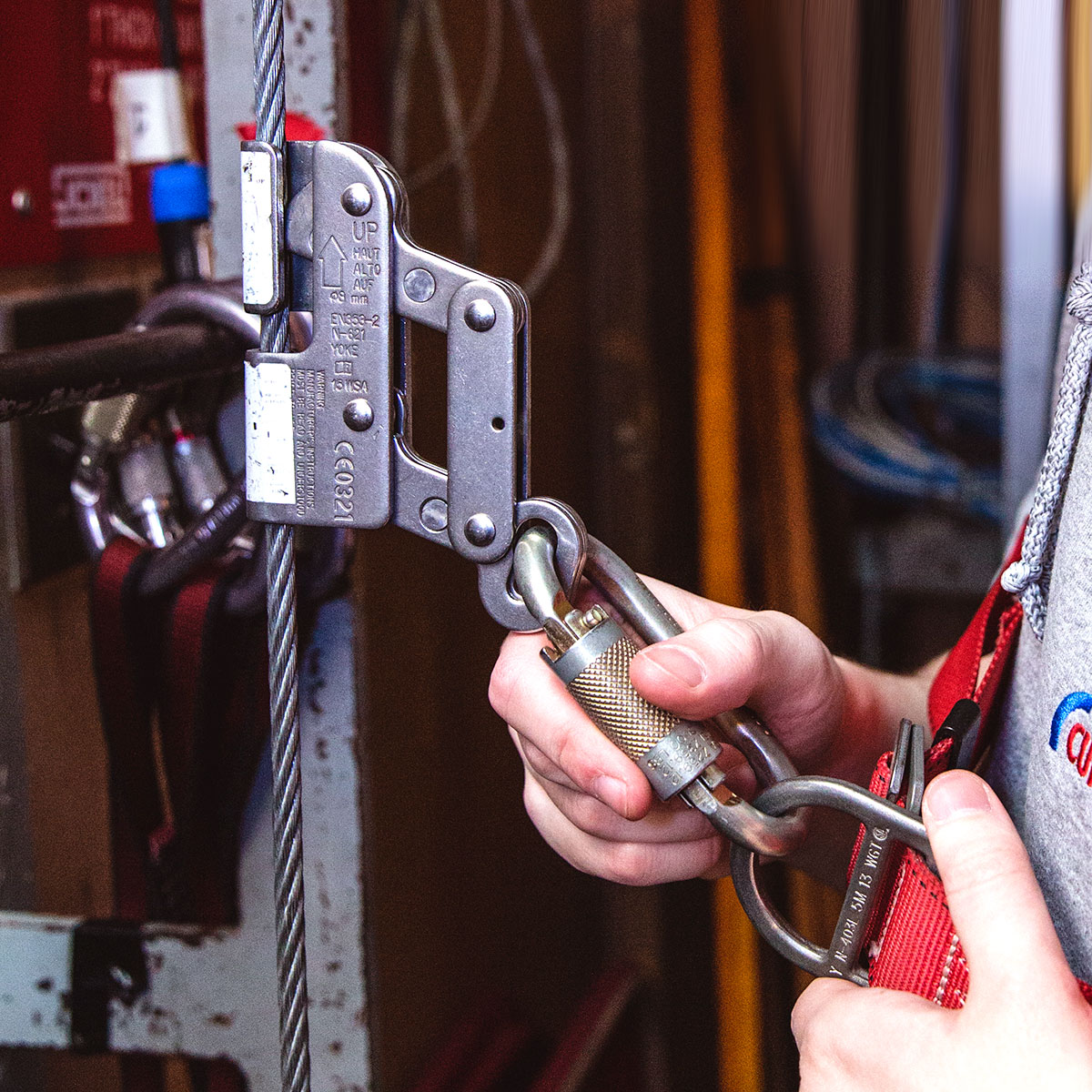 A close-up of a fall arrest device on a vertical safety line being attached to a harness with a locking carabiner.