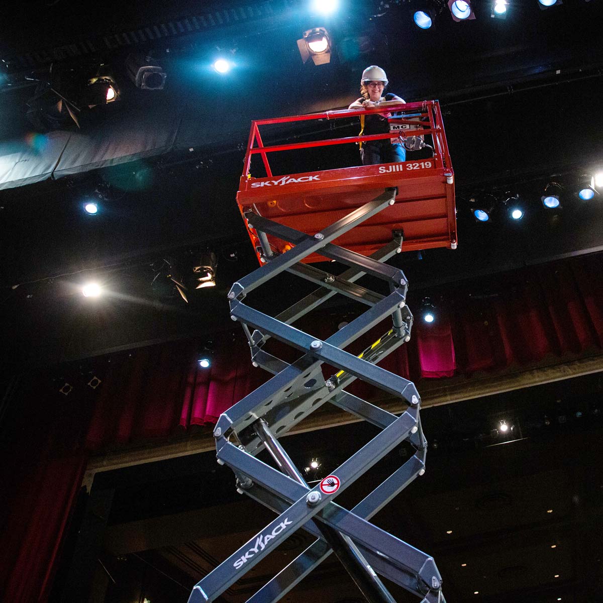 A scissor lift uses hydraulics to lift a student up to the lighting grid of the theatre in Kerr Hall.