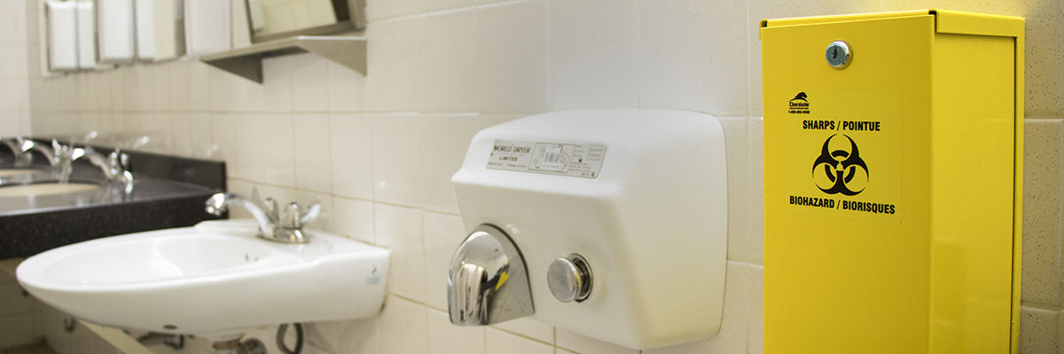 Sharps disposal container mounted on the wall in a restroom.