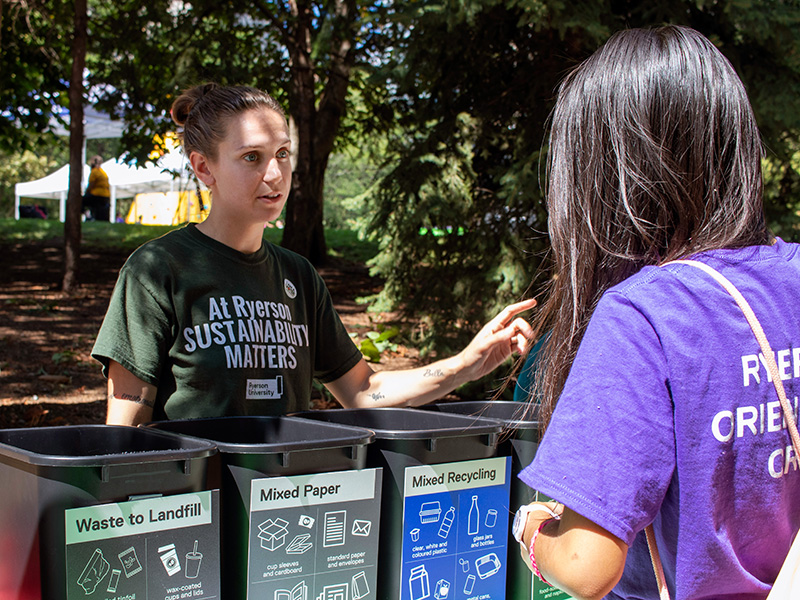 Two people speaking about the four-stream waste bins at an Orientation tabling event.