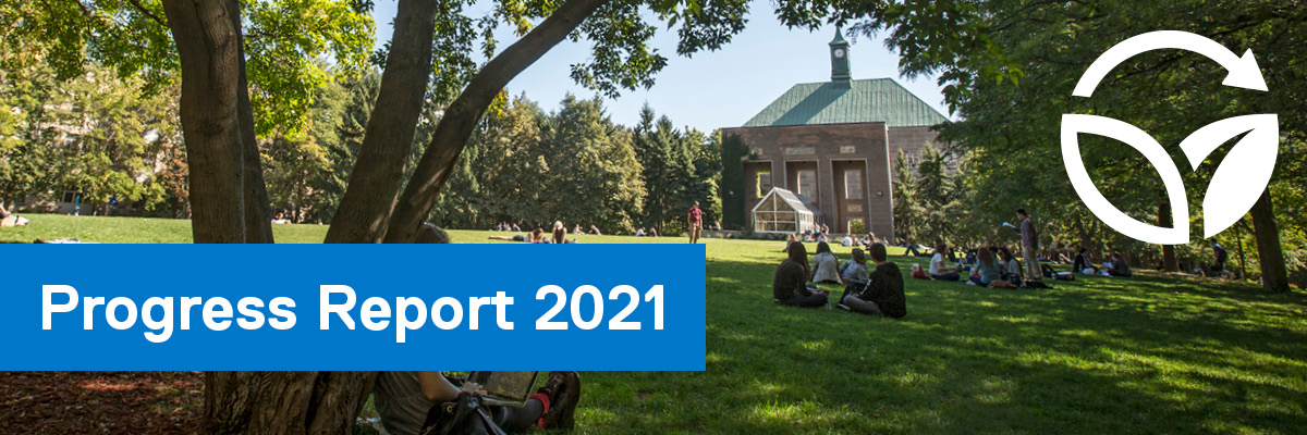 Students sitting on the green grass in the Quad with the clock tower in the background.