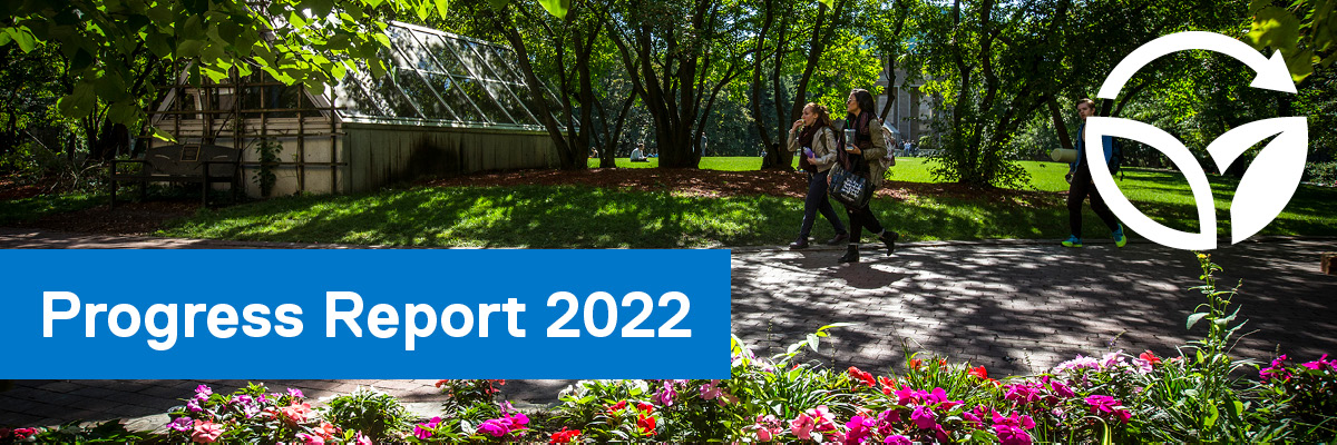 Students walking through the Quad on a sunny day with green trees and colourful flowers.