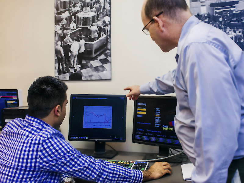 A teacher stands over a student working on a computer and points at the screen
