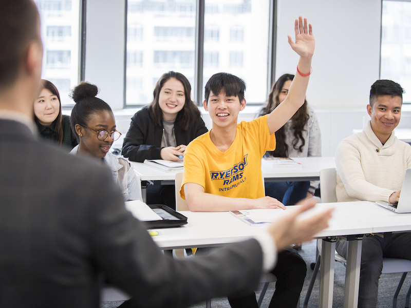 A student in a yellow shirt raises his hand in class