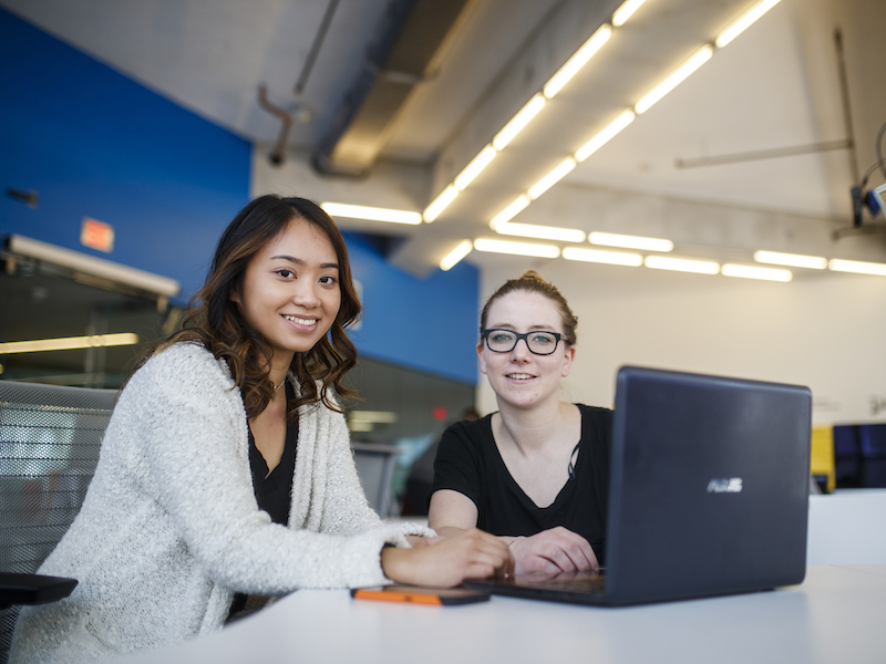 Two women in front of a laptop smiling