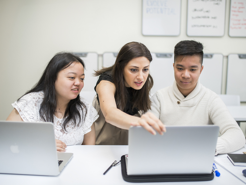 A professor explaining something to a student. Both looking at the desktop screen.