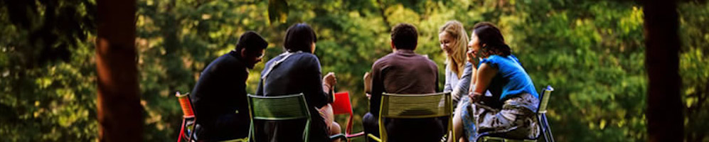 A group of people sitting on chairs in a circle in a park