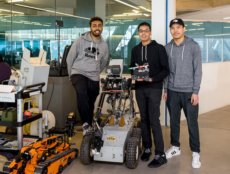 Three students stand with a robot