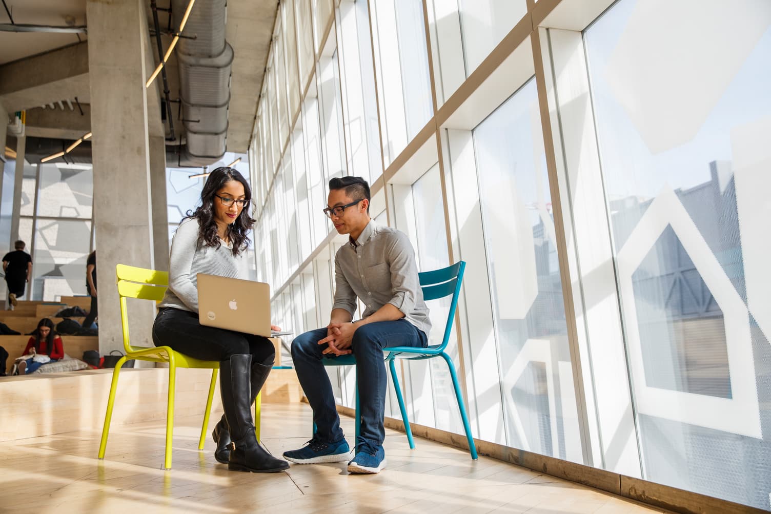 Two faculty members sit on chairs in the SLC looking at a computer