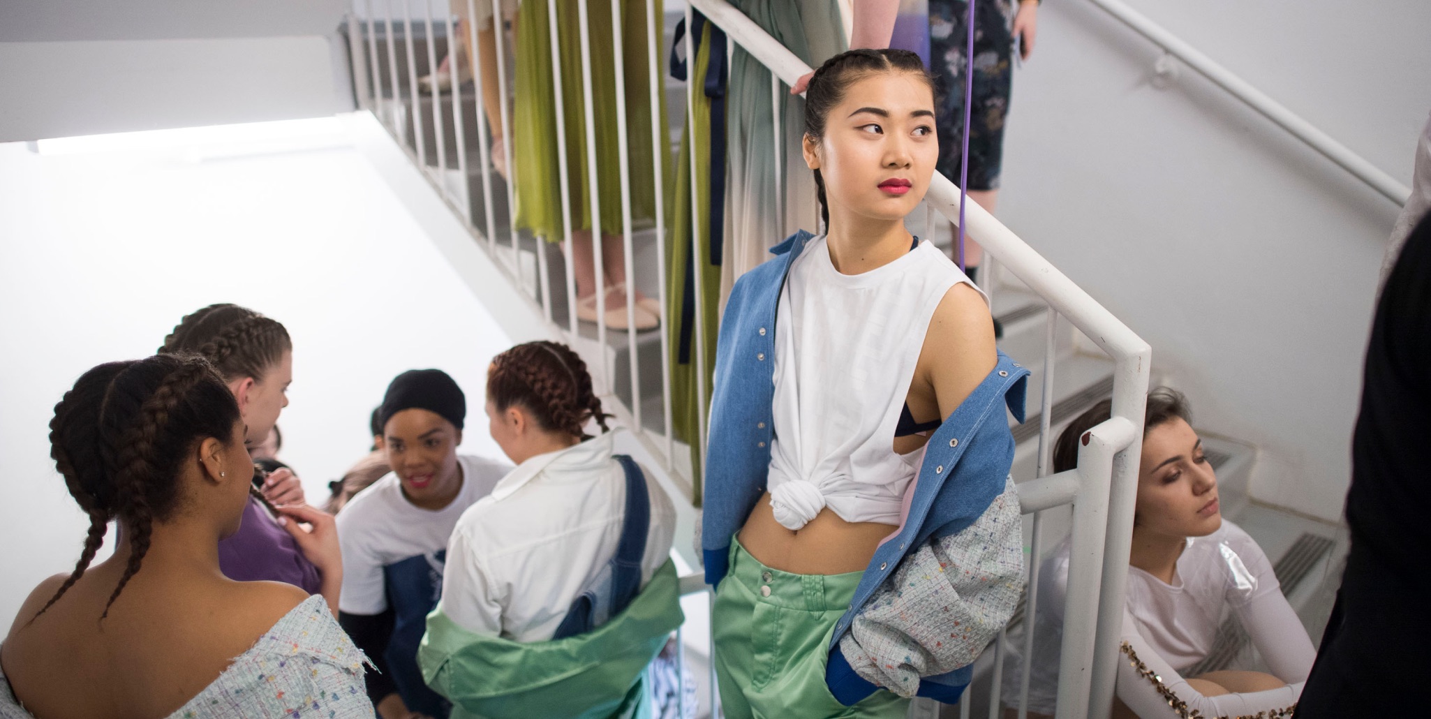 Models in casual outfits waiting on a staircase before a show.