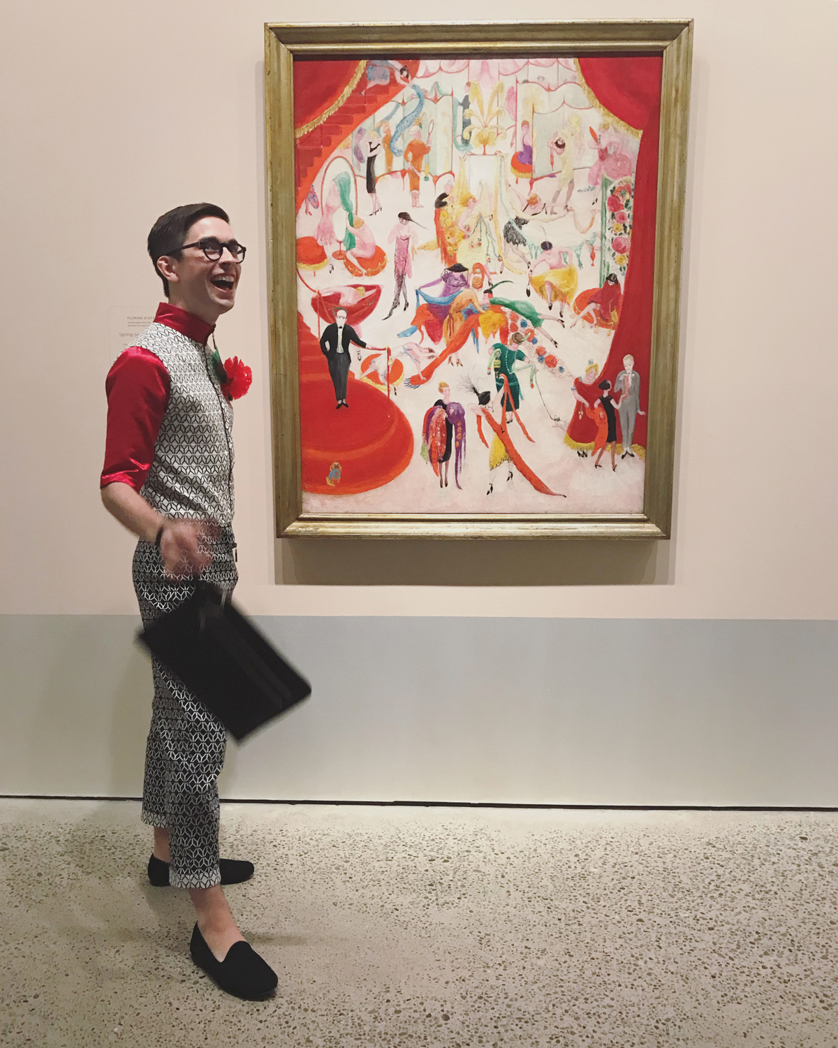 A graduate student smiling with a colourful painting in a gallery