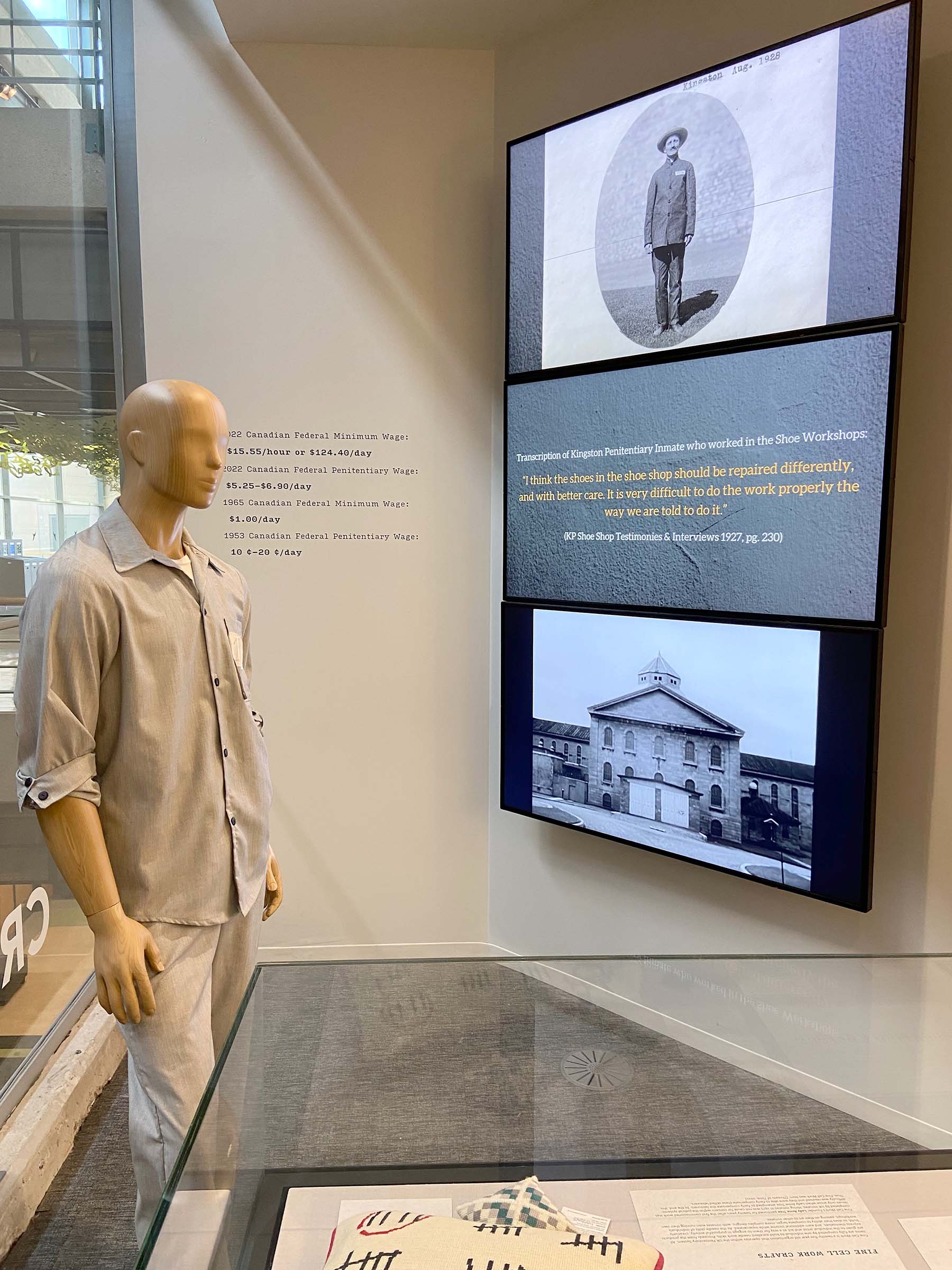 Mannequin wearing a replica of a prison uniform next to three tv screens one on top of the other displaying prison labour facts 