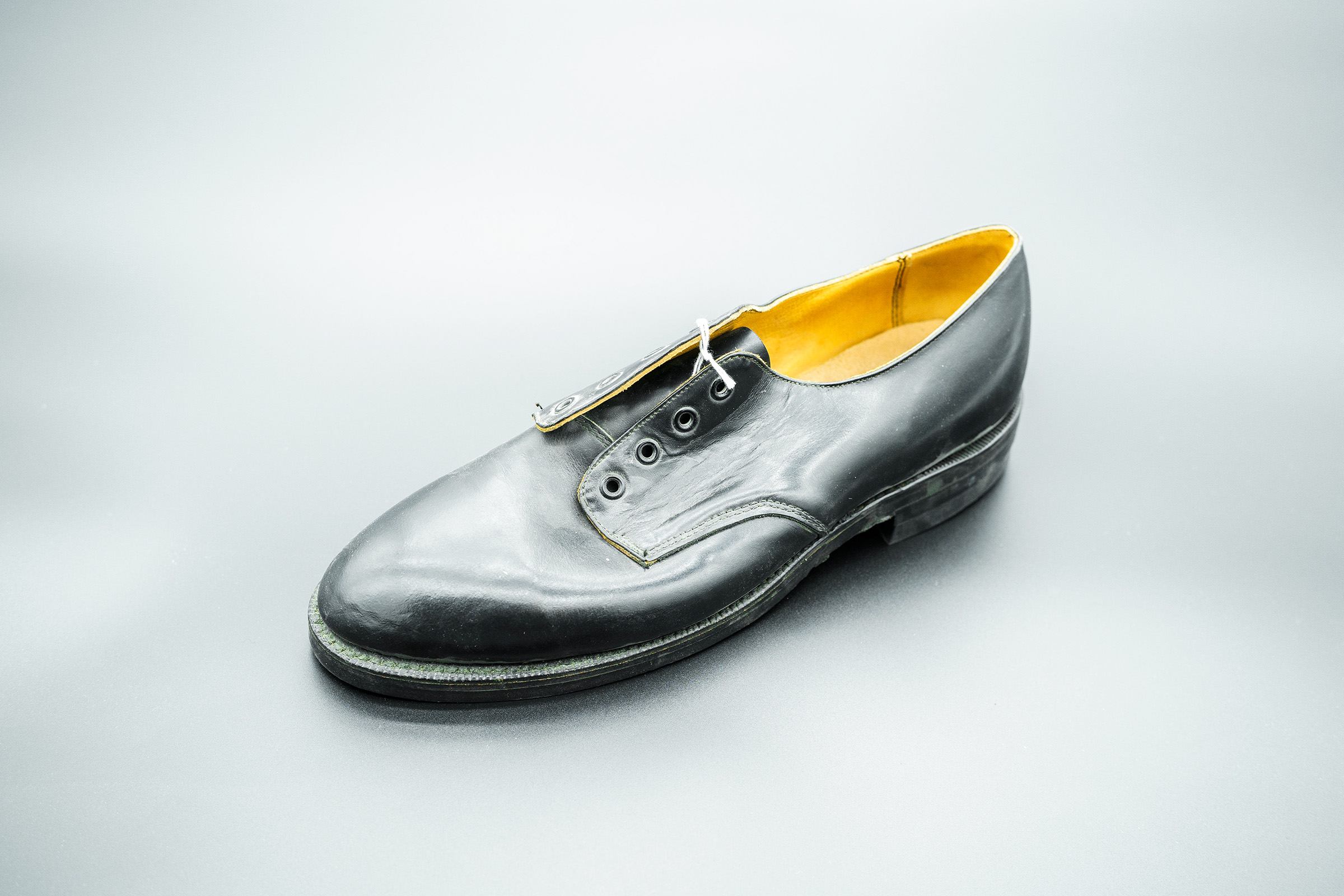A black leather oxford shoe handmade by an incarcerated person on a grey background 