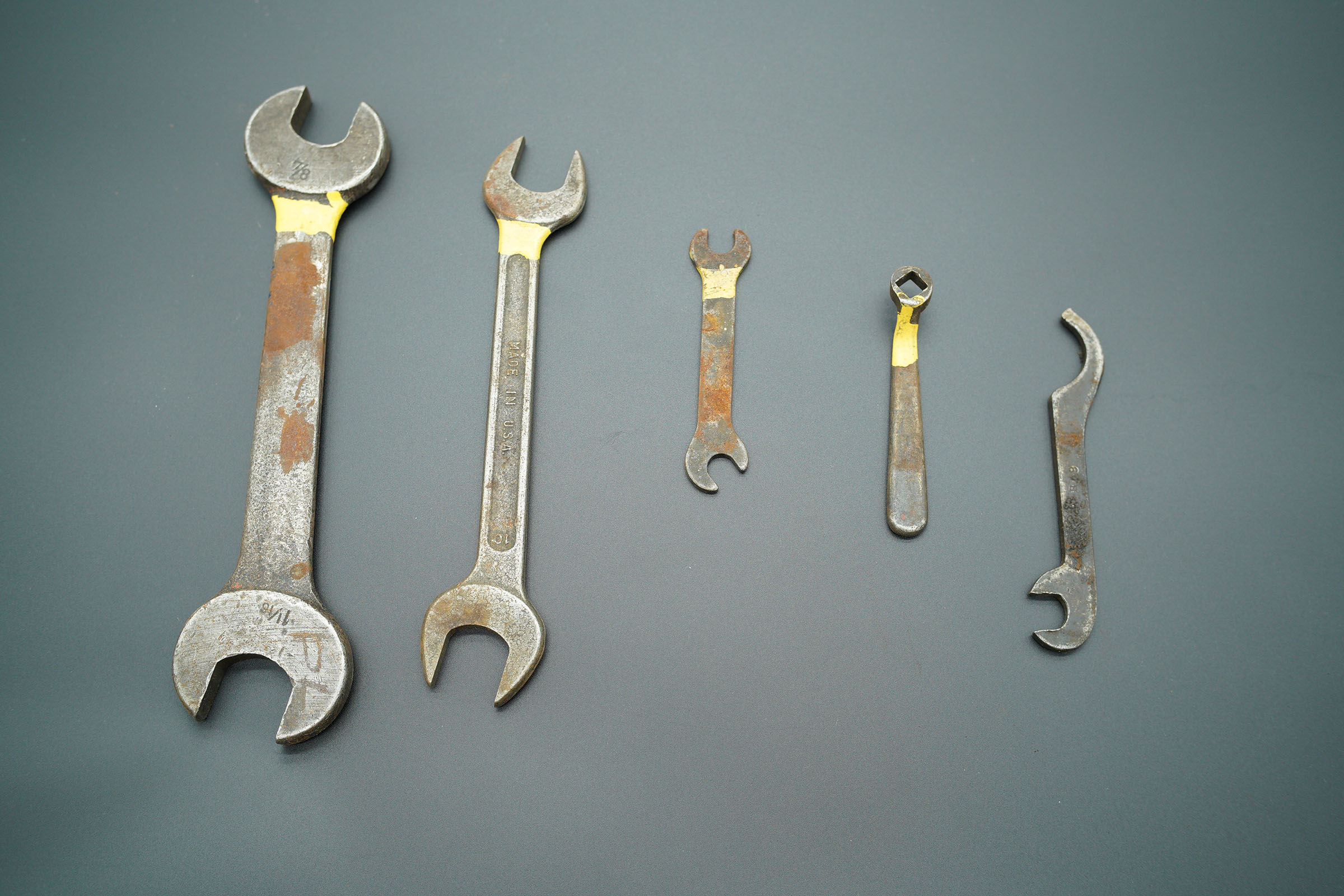 Five wrenches of varying sizes laid on a grey background, all of the wrenches have some rust 