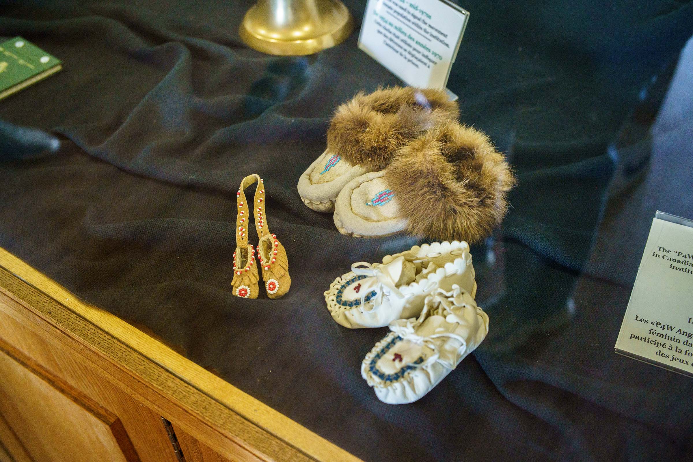 Close up of two pairs of children’s moccasins and one pair of tiny moccasins created by incarcerated people