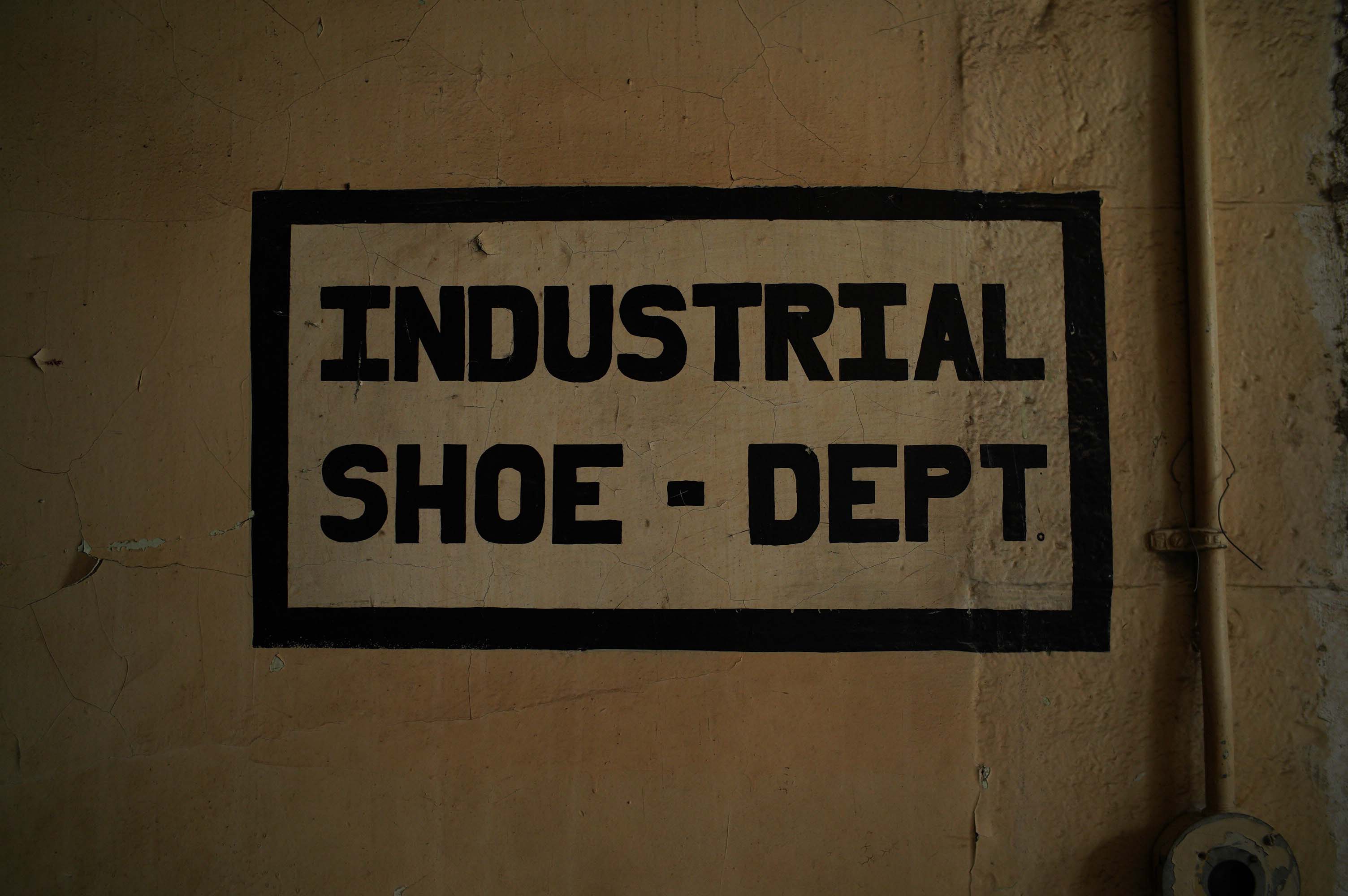 Industrial Shoe — Dept sign painted on a wall. The letters are in thick black blocky letters. 