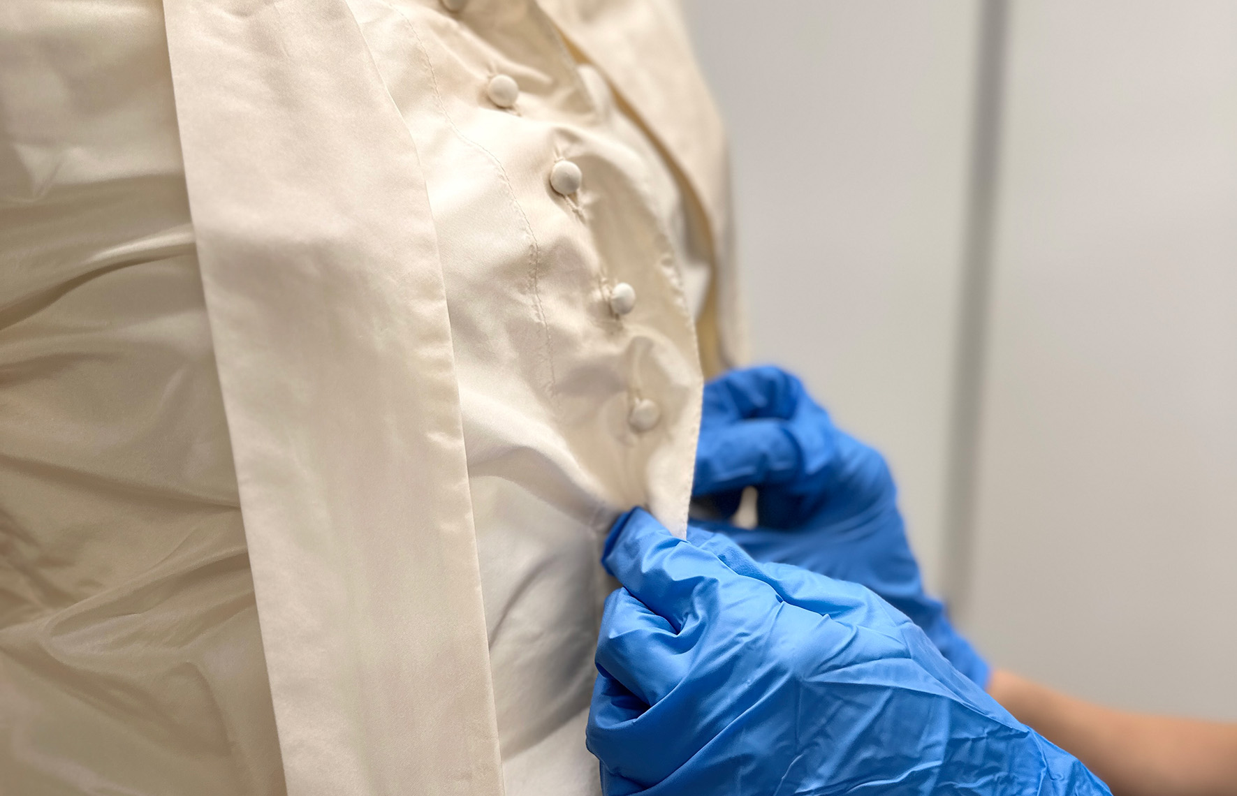 Close up of gloved hands buttoning up a blouse 