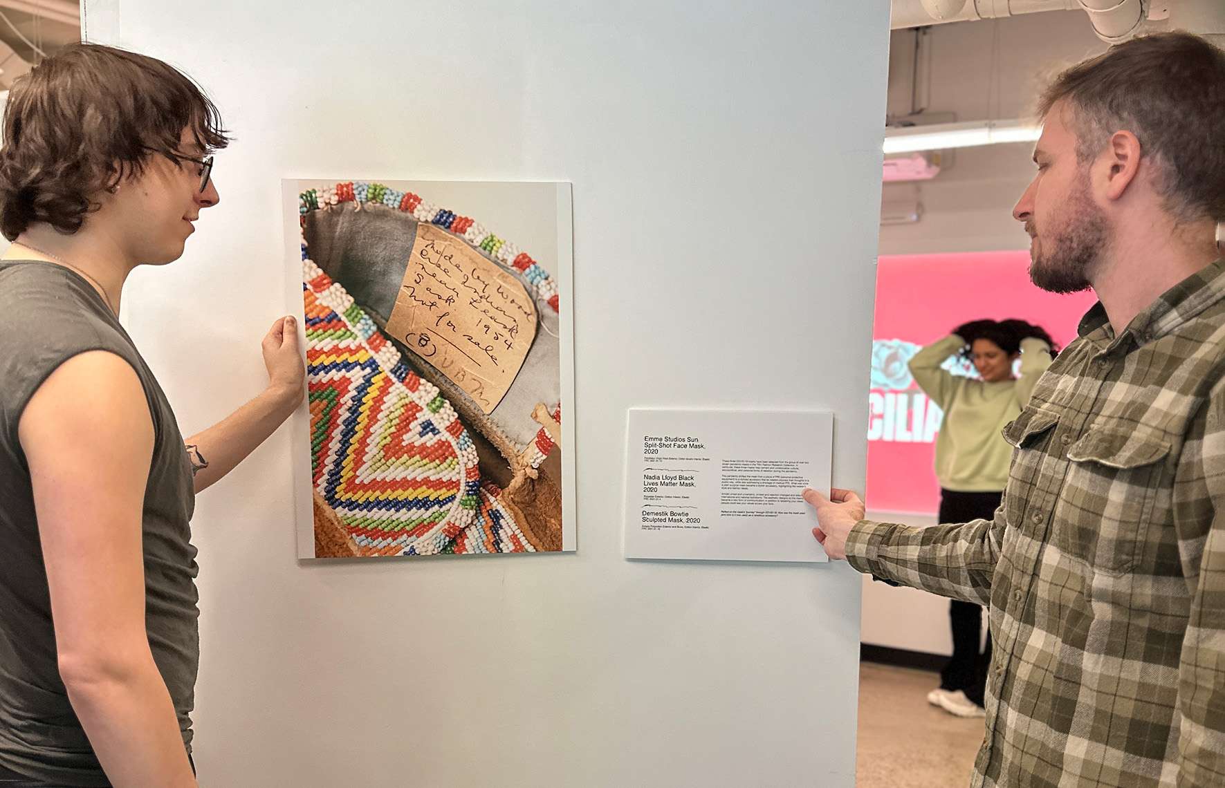 Two people setting up photo and plaque of wood cree moccasin on white panel 