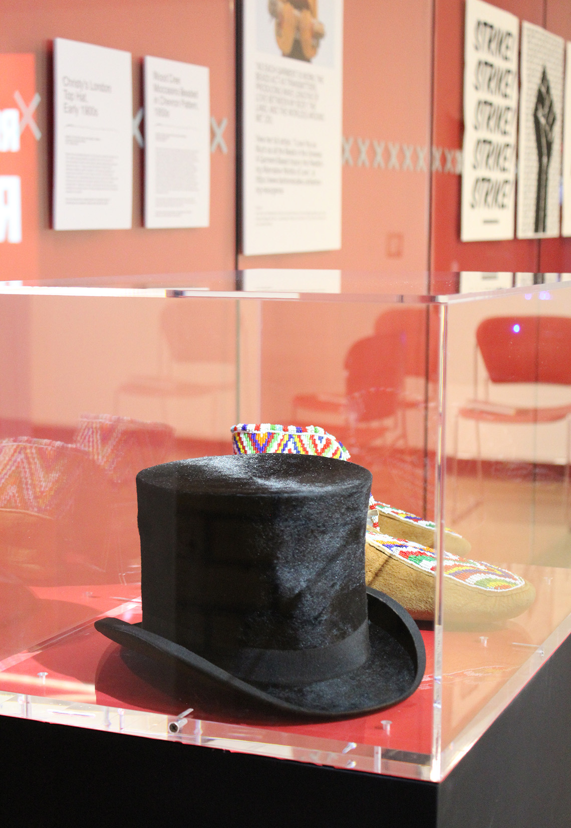 Black top hat and wood Cree moccasins in a glass case. 