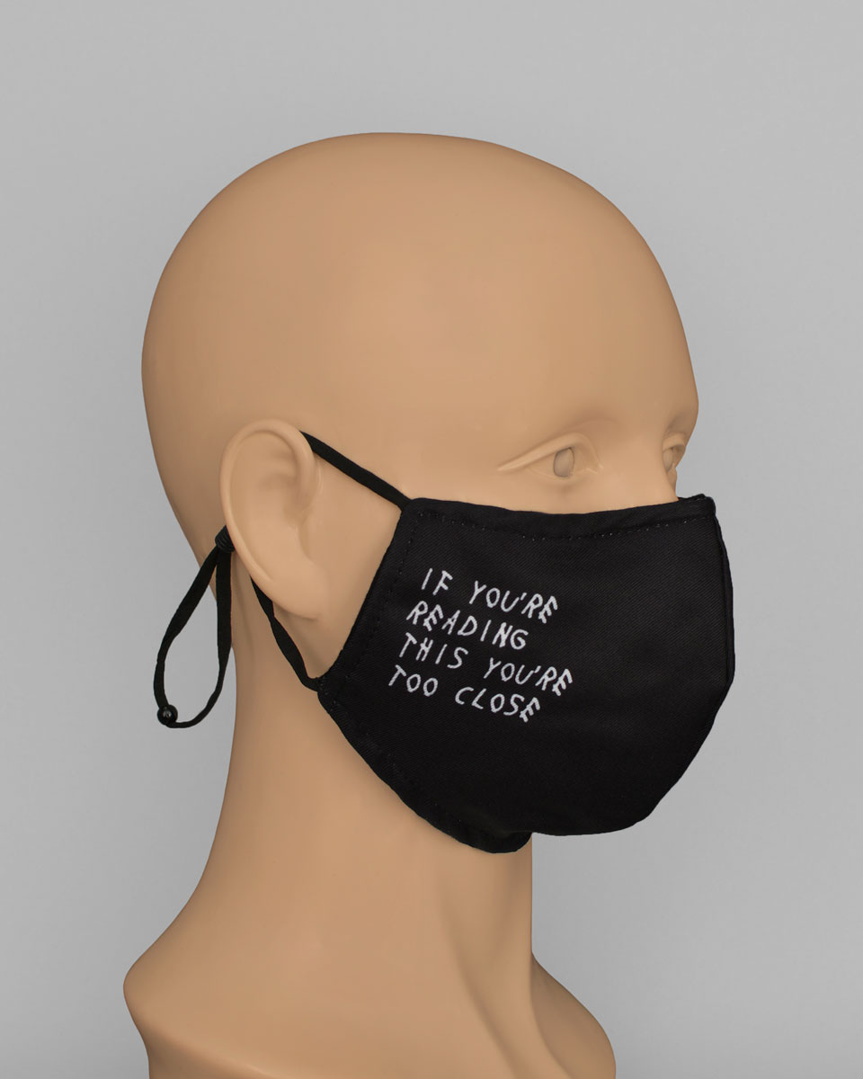 Side view of a mannequin head wearing a black mask that reads "if you're reading this you're too close"