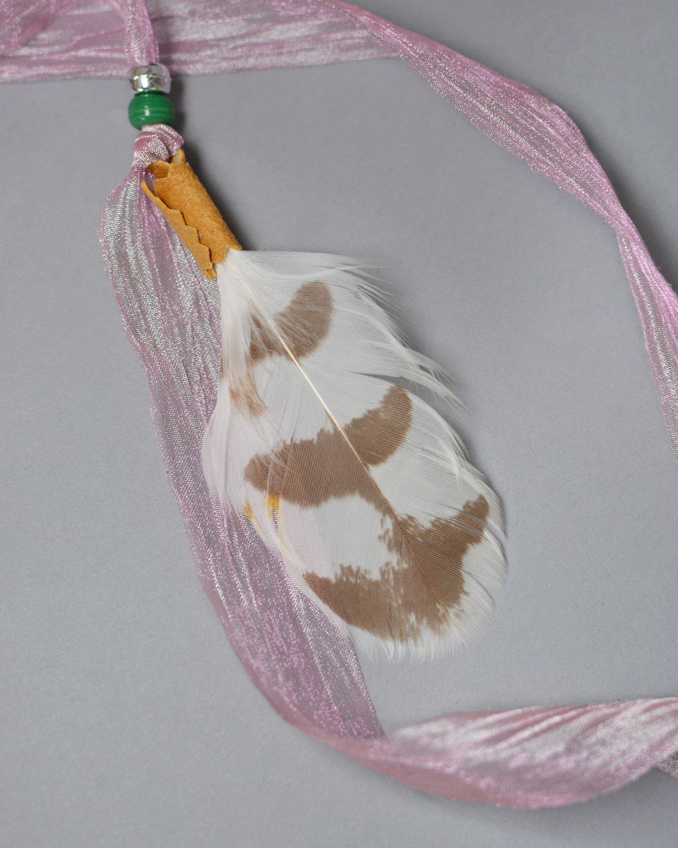 Decorative ribbon and feathers that hang from the side of the face mask