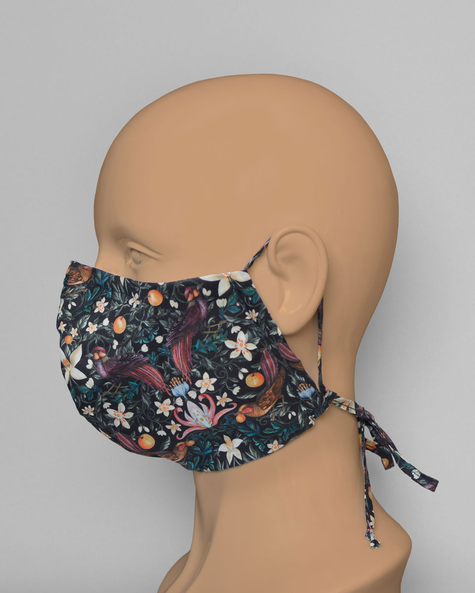 Side view of a mannequin head wearing a black mask with a fruit, floral and bird print