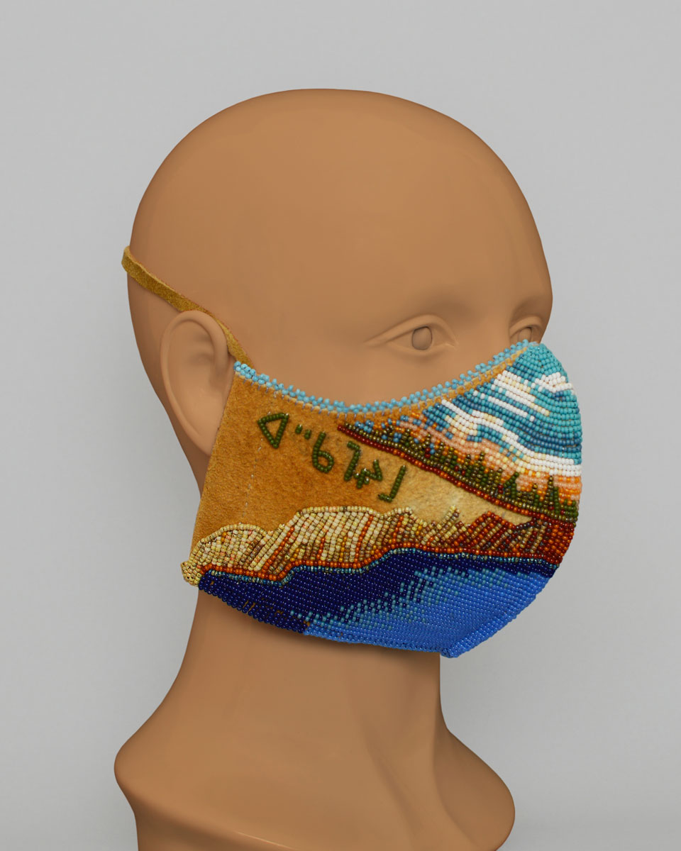 Side view of a mannequin head wearing a leather mask with a beaded landscape with Cree syllabics