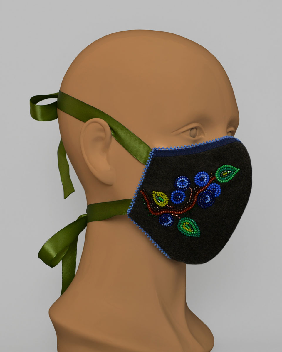 Side view of a mannequin head wearing a blue face mask with a beaded blueberry design with green ribbon ties