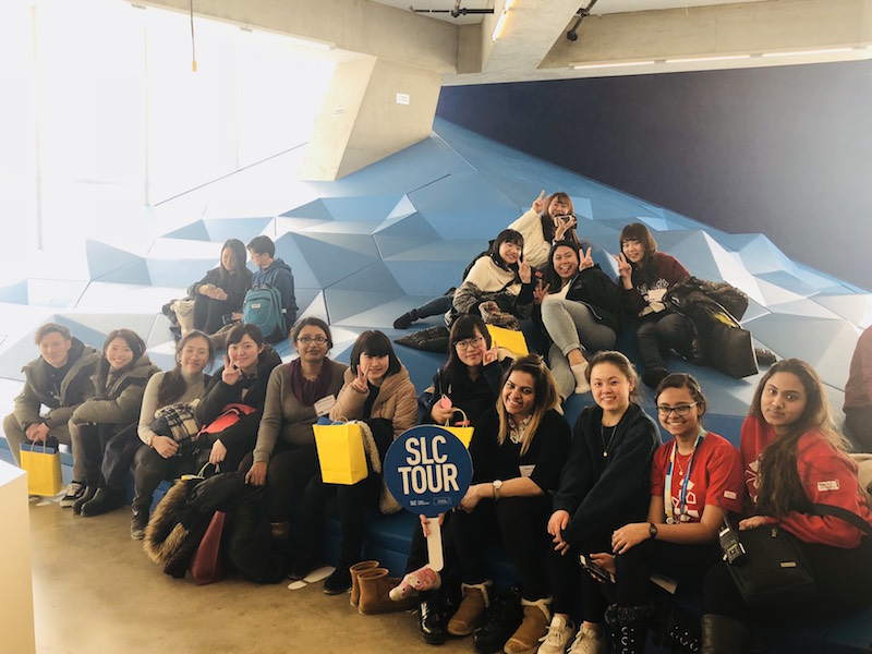 Group of students sitting down inside SLC holding a sign which reads 'SLC TOUR'