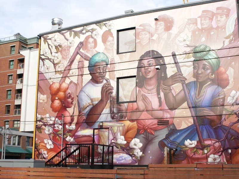 Urban on side of building depicting youth in colourful clothing singing and playing instruments
