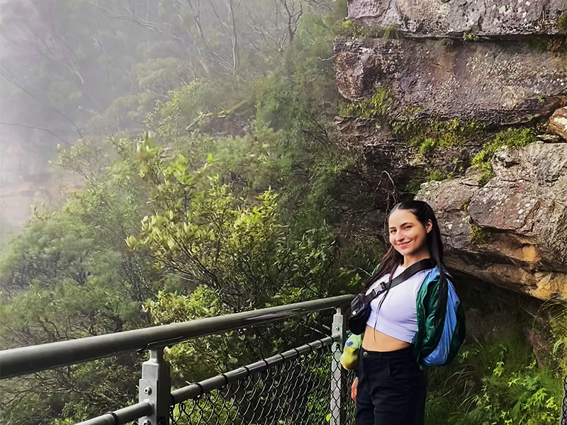 Laura Pietroiusti poses for the camera in front of a railing and a forest behind her