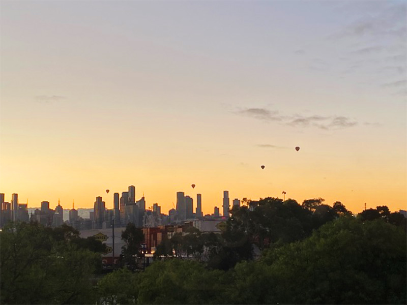 A city skyline with hot air balloons rising above it 