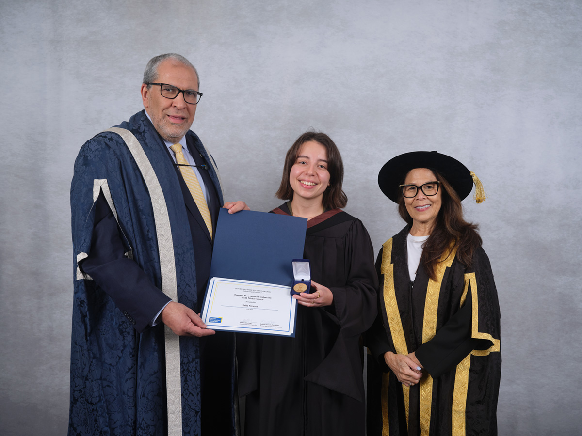 Julia Menezes poses with degree and gold medal, flanked by TMU's president and chancellor