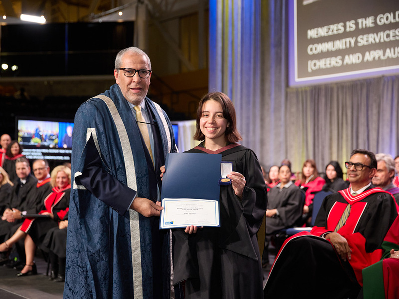 Julia Menezes displays her Gold Medal on the convocation platform with TMU's president.