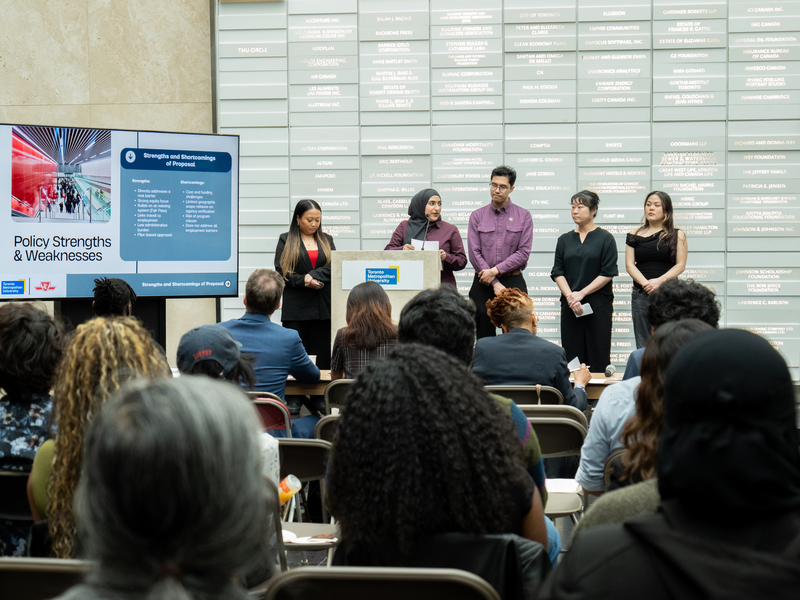 A five-student team presents on stage.