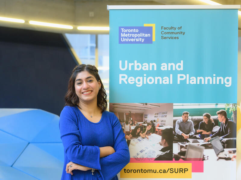 Sidra Asif stands in front of a banner featuring Urban and Regional Planning at TMU