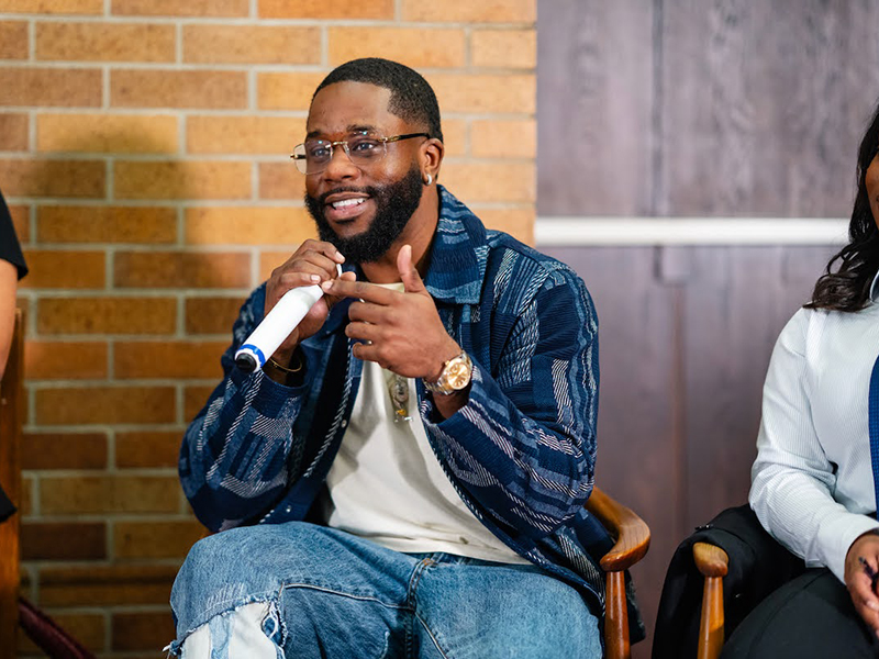 Professor Travonne Edwards, seated, speaks into a microphone at an event