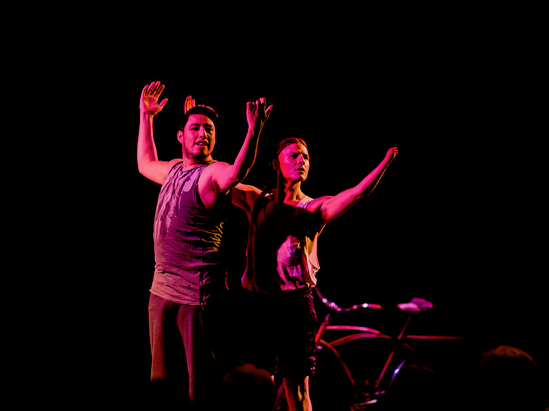 Performative dancers standing in pink spotlight while striking expressive poses 