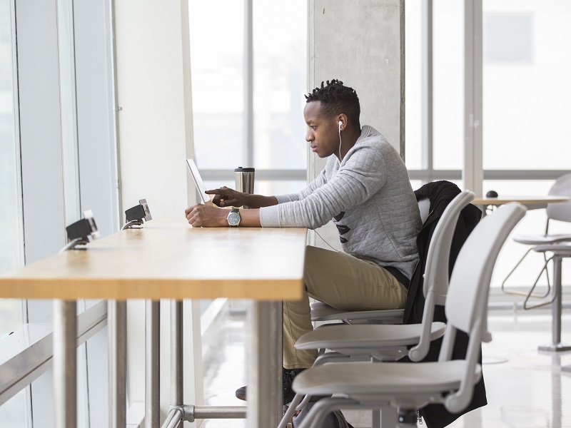 Side view of a man seated at a desk looking at a laptop.