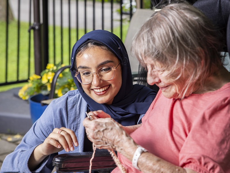 Student and resident visit outdoors while resident knits