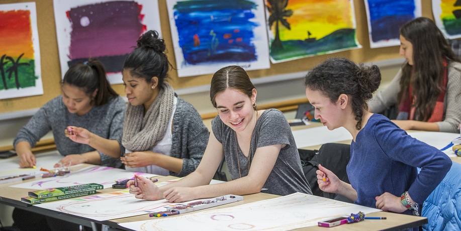 Four students in a classroom drawing pictures with pastels