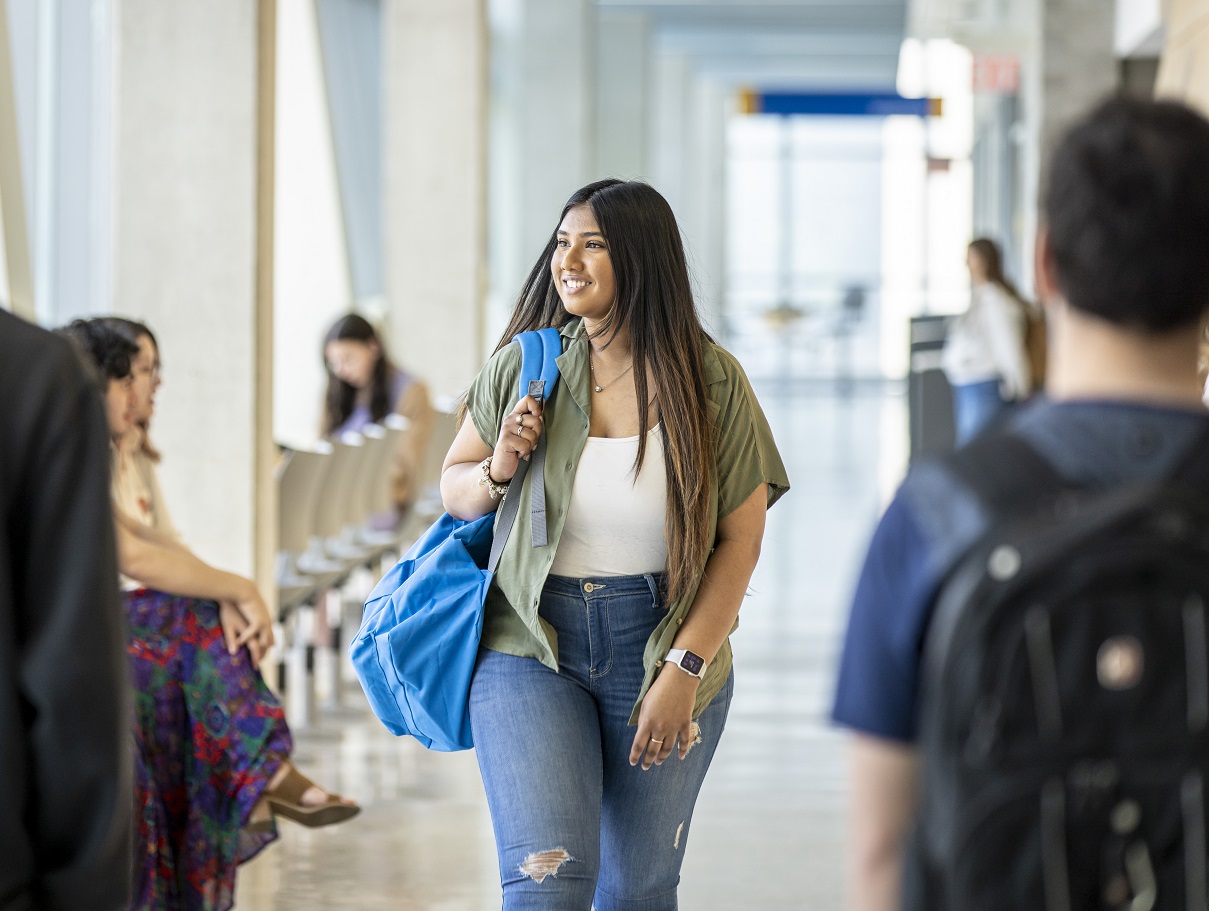 Smiling student walking through a corridor with tote bag