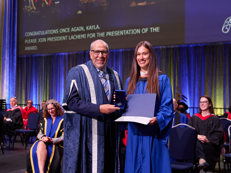 Kayla Longland on the convocation stage receives her 2026 TMU Gold Medal from President Lachemi