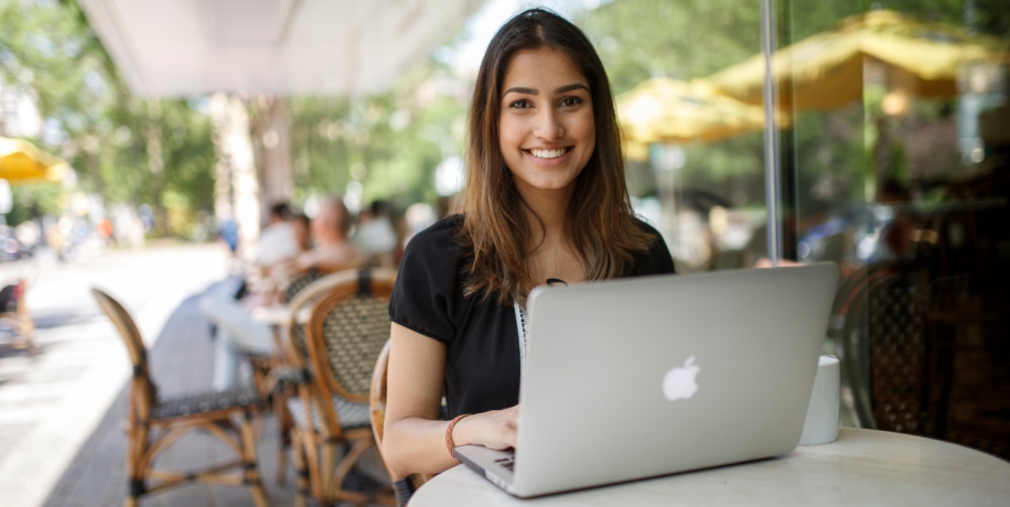 Smiling student sitting at coffee shop with open laptop