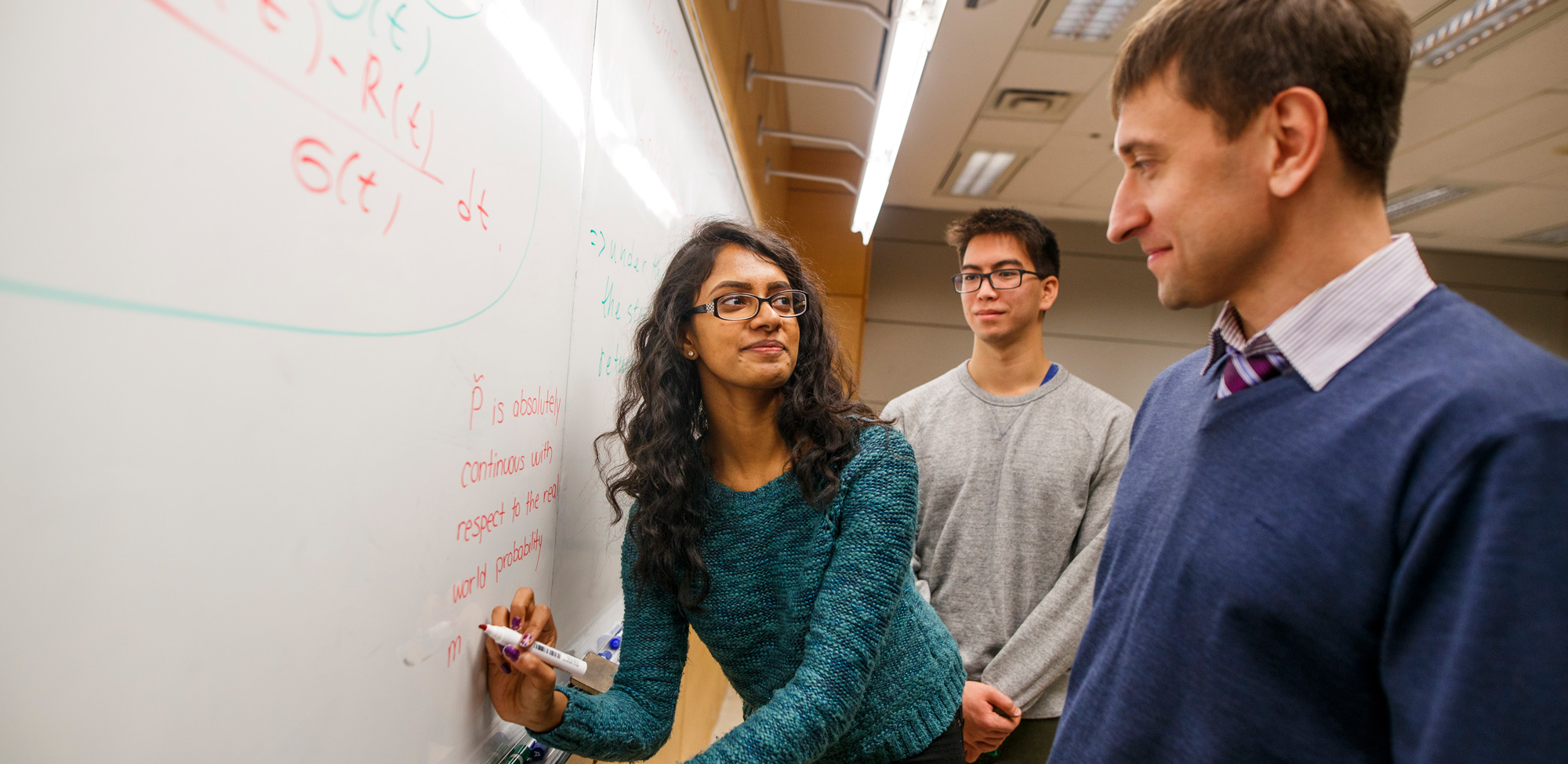 Student and professor solving financial math equation at white board.